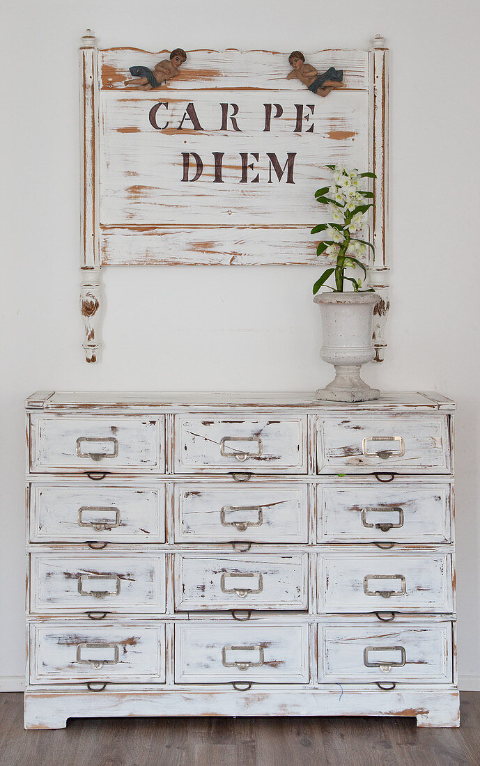 Old bed headboard with lettering on wall above chest of drawers