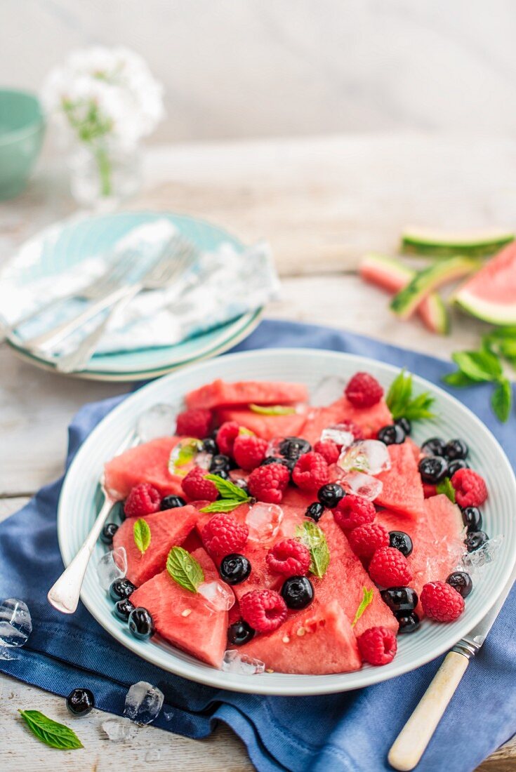 Fruit plate with watermelon slices, raspberries and blueberries with mint and ice cubes