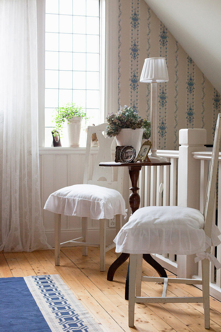 Two white chairs with ruffled seat cushions at antique side table