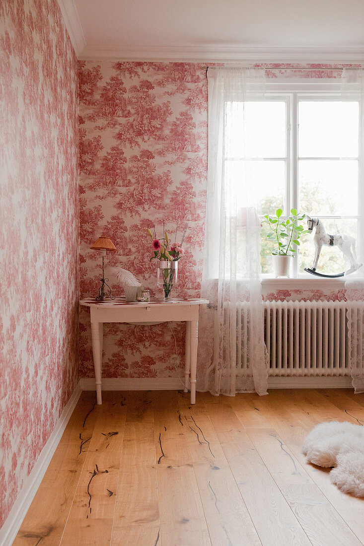 Small table next to window in bedroom with red toile de Jouy wallpaper