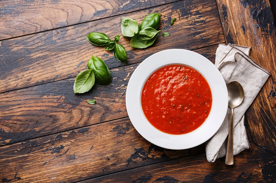 Tomatensuppe mit Basilikum in Teller auf Holzuntergrund (Aufsicht)