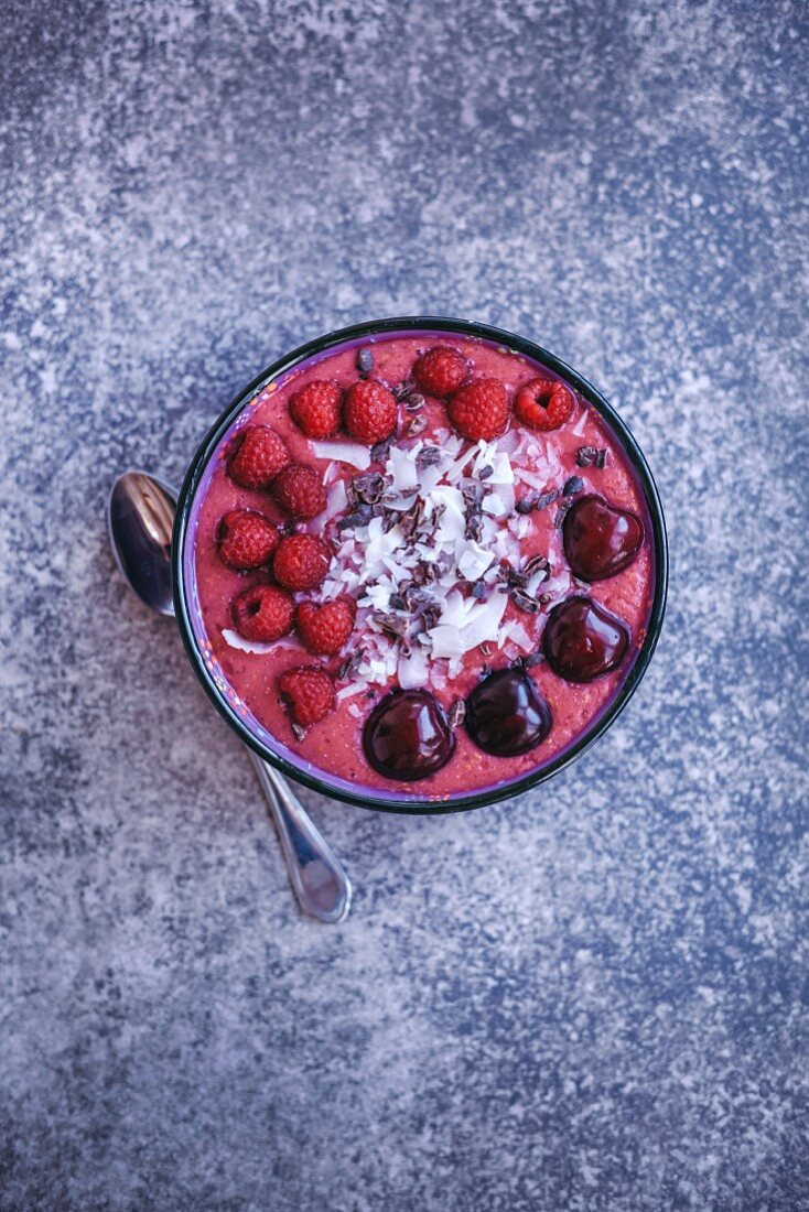 Raspberry smoothie bowl topped with fresh raspberries, cherries, coconut flakes and cacao nibs