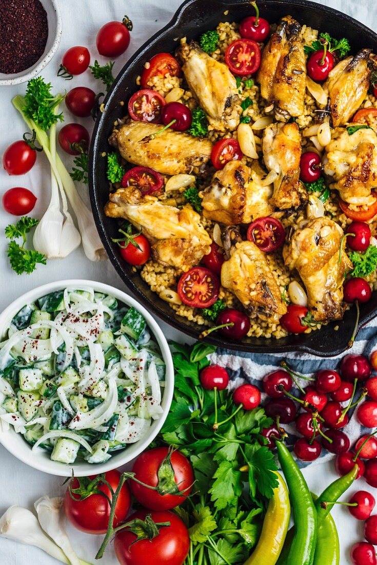 Bulgur-Pilaf mit Chicken Wings, Kirschen und Tomaten serviert in der Pfanne