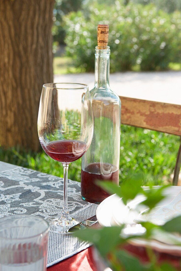 Glass of wine next to bottle of wine on garden table