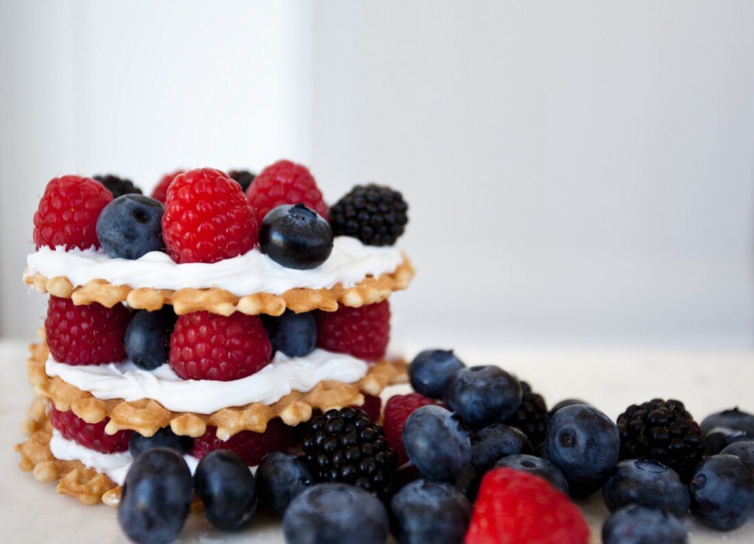 Stacks of wafer cookies, icing and mixed berries with a white background