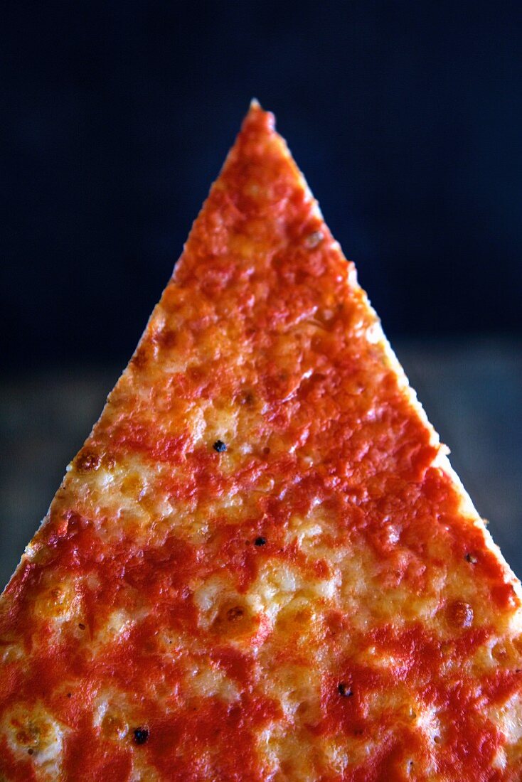 A slice of pizza in front of a dark background (close-up)