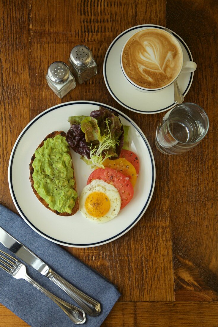 Frühstück mit Avocadobrot, Spiegelei, Tomaten und Tasse Kaffee