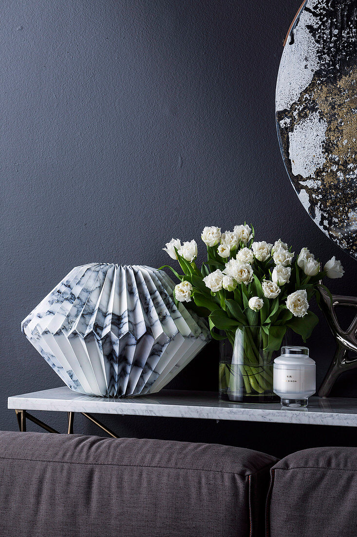 Console table with marble paper sculpture and bouquet of tulips, behind couch