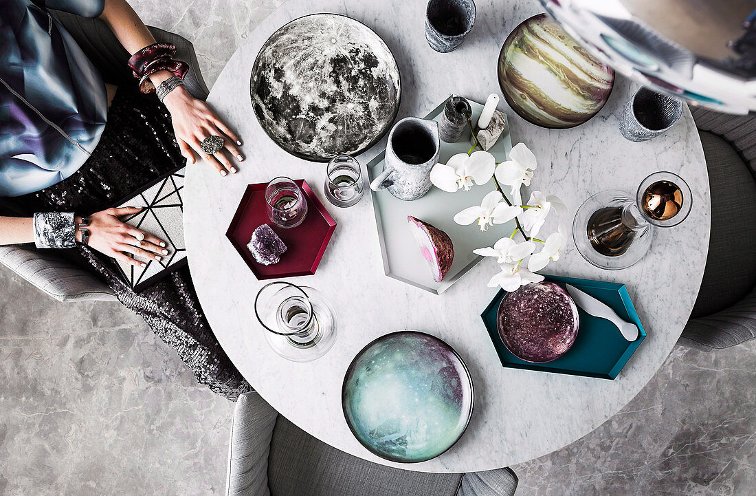 Frau sitzt am runden Marmortisch mit Geschirr und Orchidee