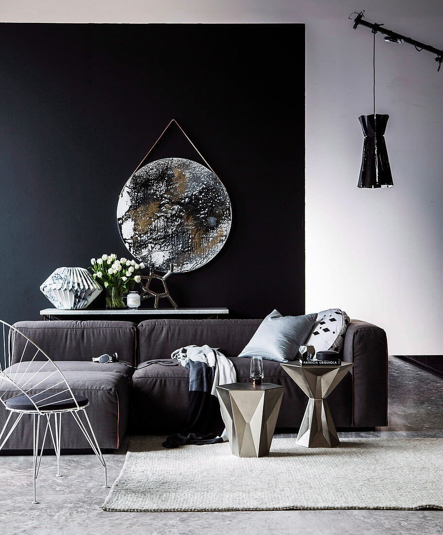 Chair, silver side tables and sofa in front of console table with sculpture made of marble paper and bouquet of tulips, round artwork with a metallic look