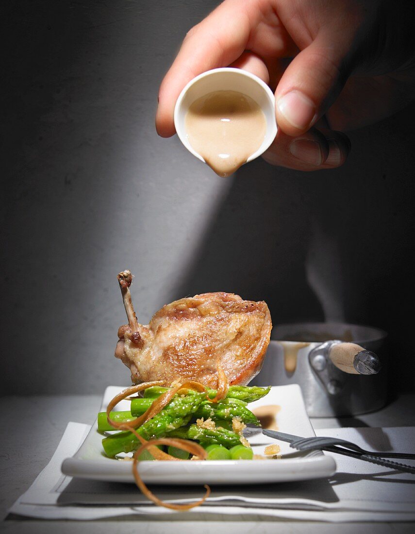 Hollandaise sauce being poured over quail breast and green asparagus