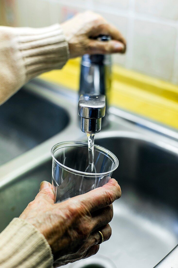 Elderly person using a tap for drinking water