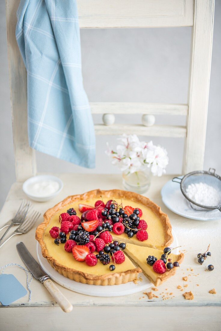 Vanilla tart decorated with fresh summer berries, with a slice cut out