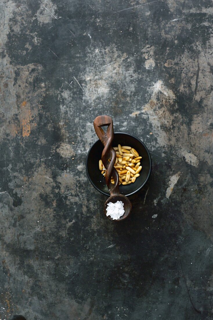 Roasted pine nuts in a bowl and salt crystals on a wooden spoon