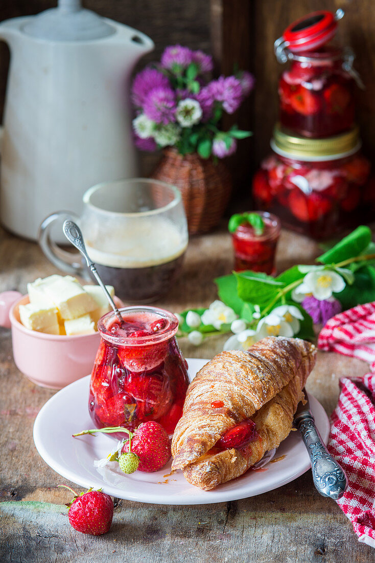 Croissant mit Erdbeerkonfitüre, Butter und Kaffee