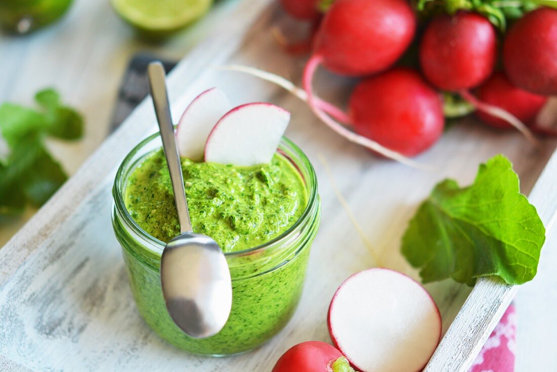 Radish leaf pesto in a glass, next to a bunch of radishes