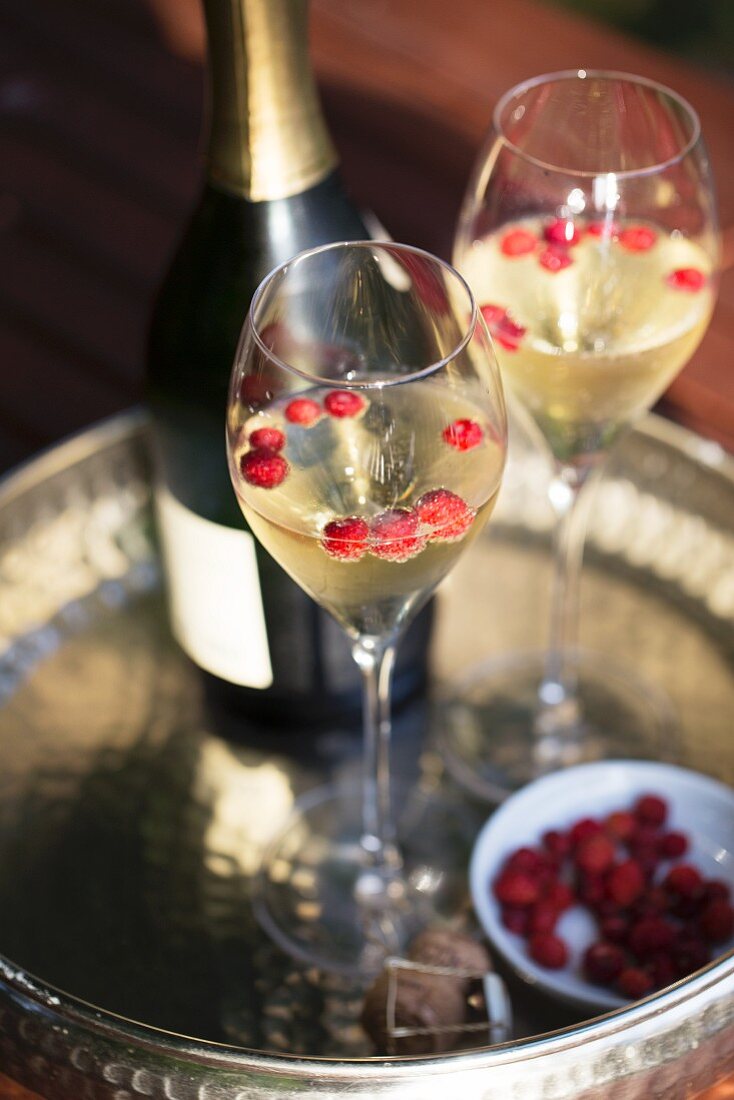 A bottle and two glasses of champagne with wild strawberries on a silver tray