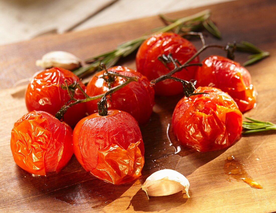 Ofengeröstete Tomaten mit Knoblauch und Kräutern auf Holzbrett (Nahaufnahme)