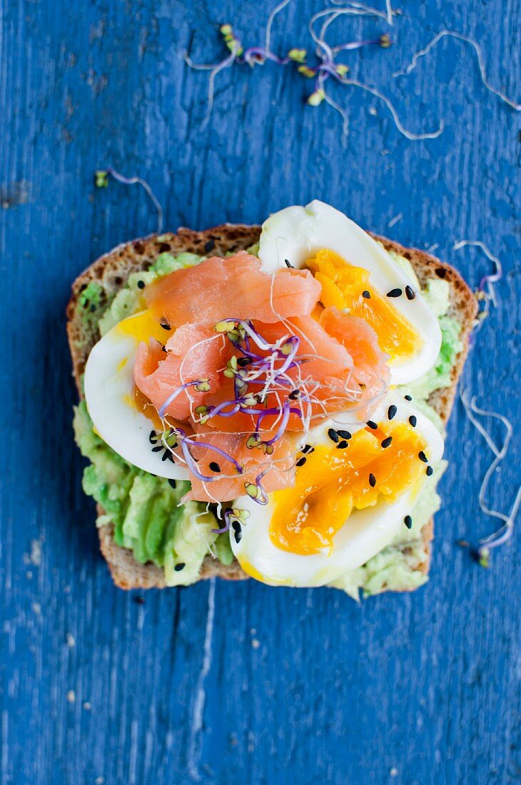An open sandwich with avocado, egg, salmon, sprouts and sesame seeds (top view)