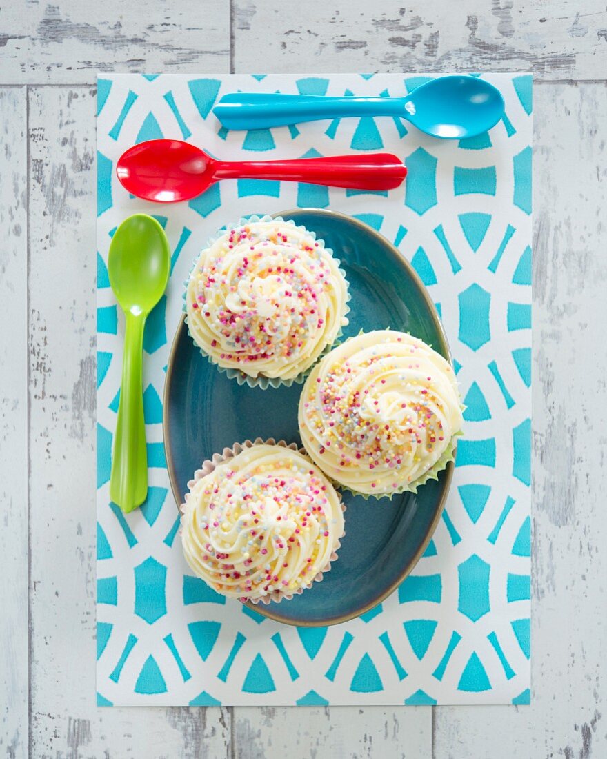 Cupcakes mit Cremehaube und bunten Zuckerstreuseln (Aufsicht)