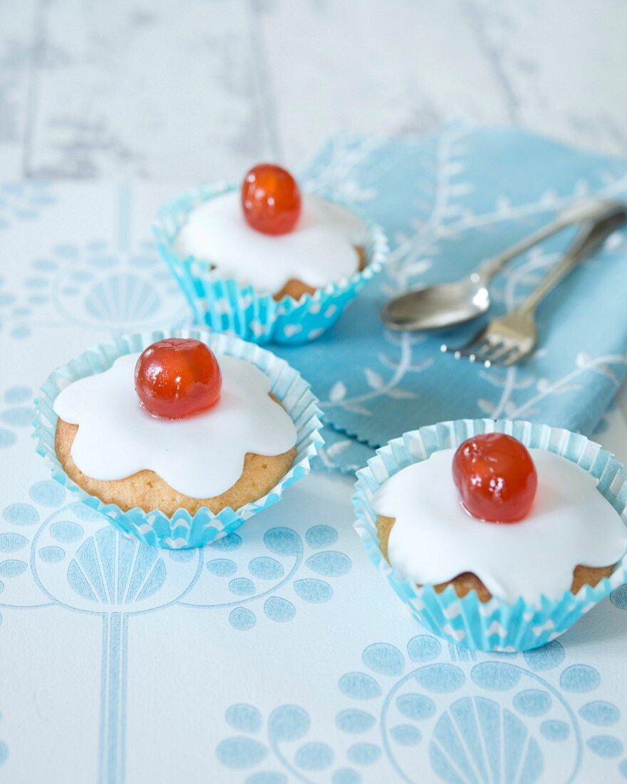 Cupcakes decorated with icing and glace cherries