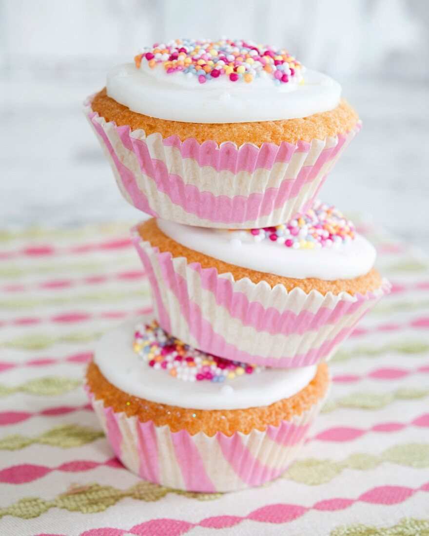 Three stacked cupcakes decorated with icing and colourful sugar sprinkles
