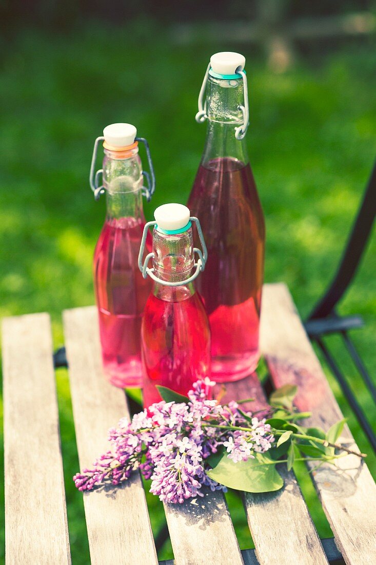 Three bottles of lilac blossom syrup in a garden