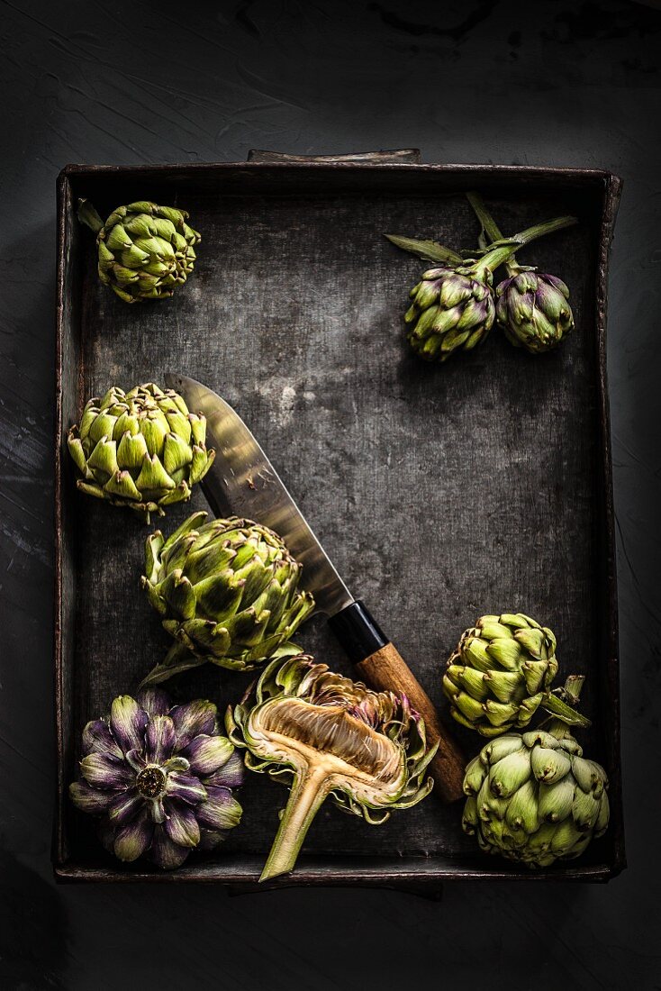Whole and halved artichokes on a black metal tray