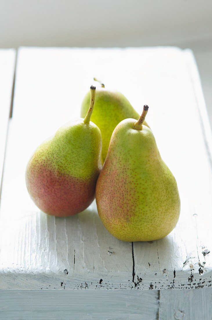 Three green pears on a white wooden background