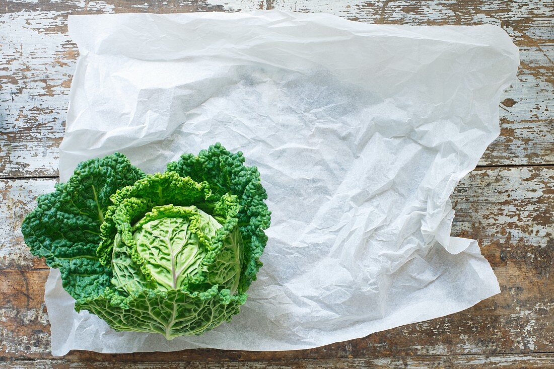 A savoy cabbage on paper and a wooden background (top view)