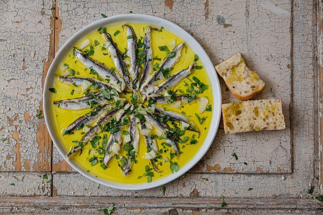 Anchovies in garlic oil served with herbs and bread (top view)