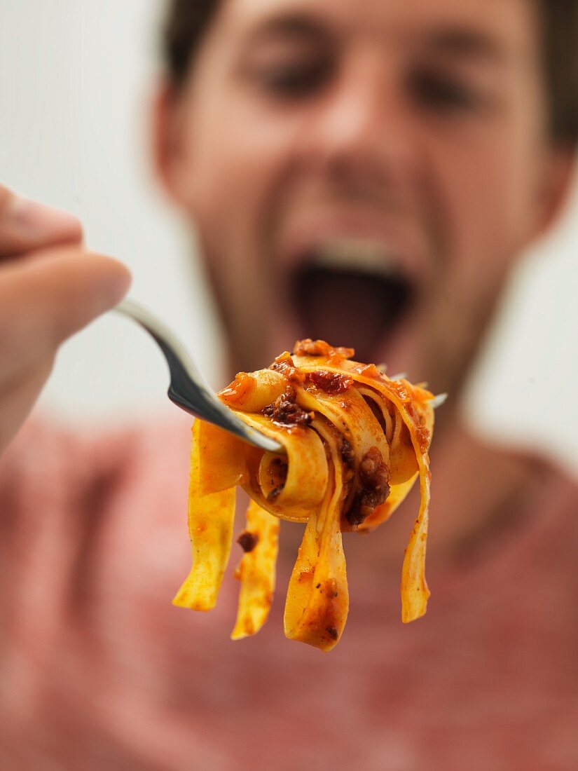 A man holding a fork with tagliatelle bolognese