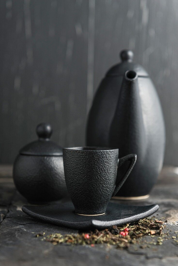 Tea in a black cup in front of a teapot and sugar pot