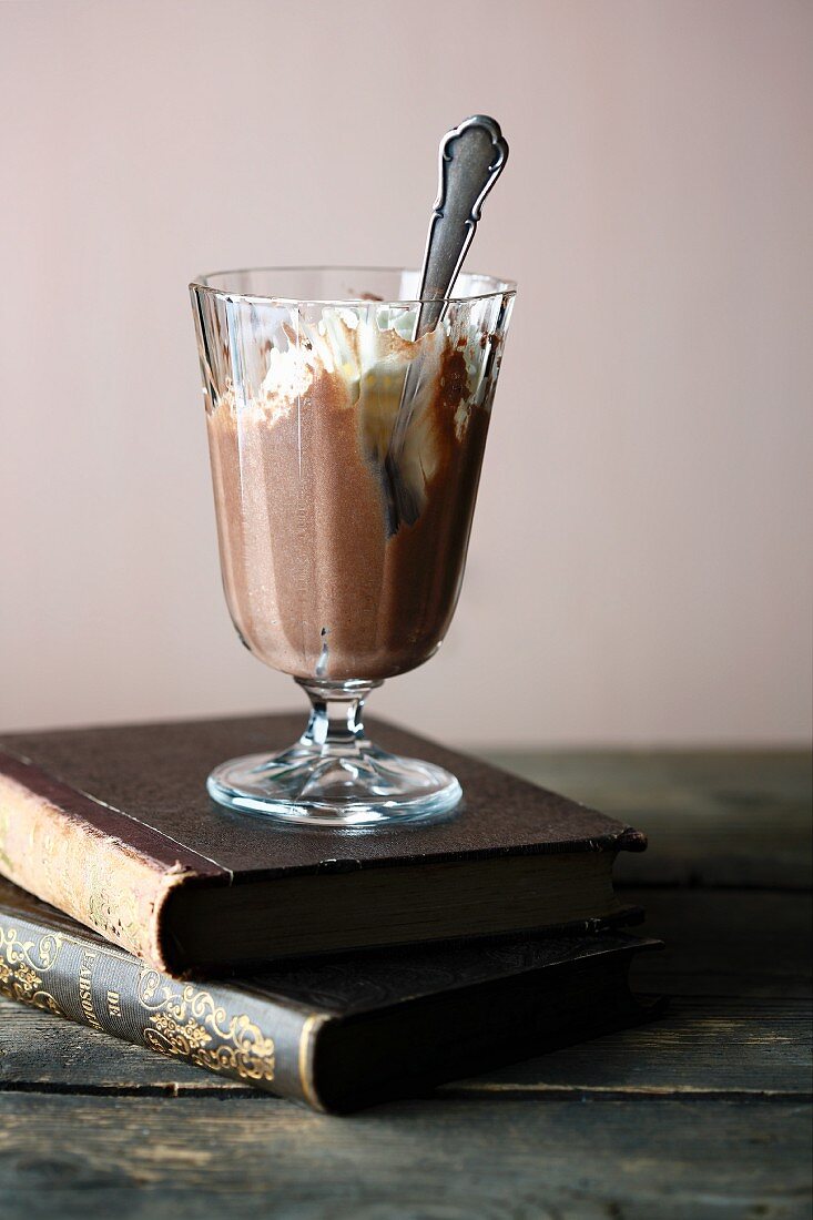 Chocolate mousse and cream in a glass with a spoon, on two old books