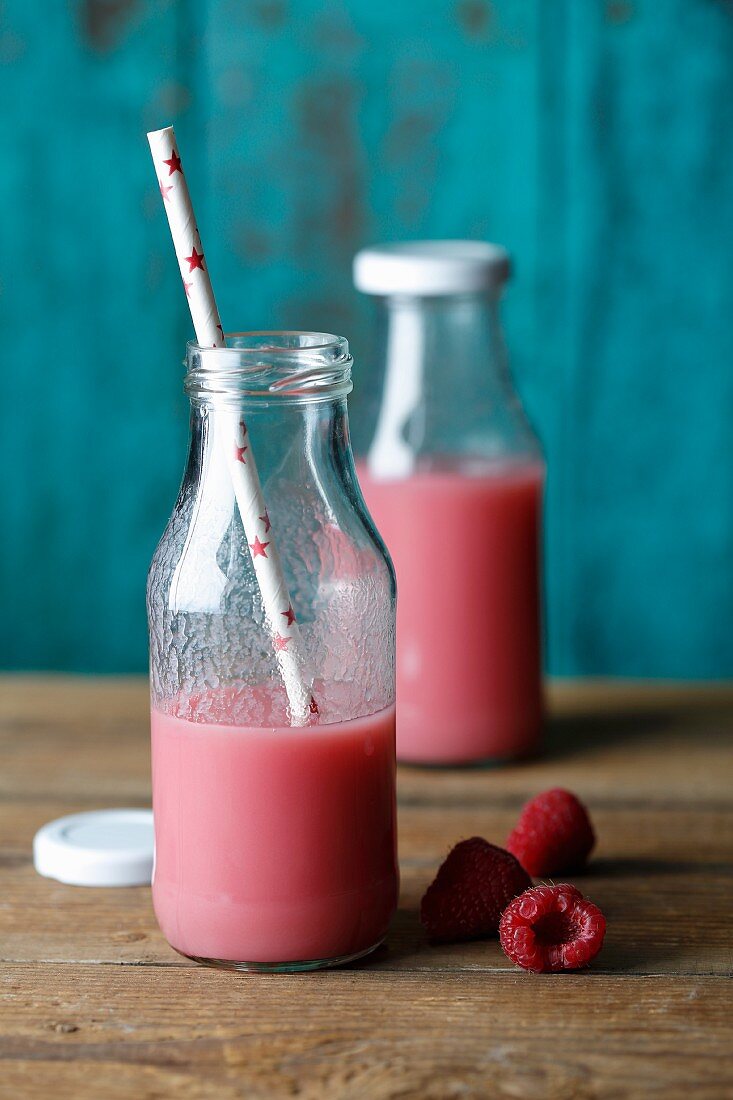 Rote Smoothies in zwei Milchflaschen mit Himbeeren und Strohhalm