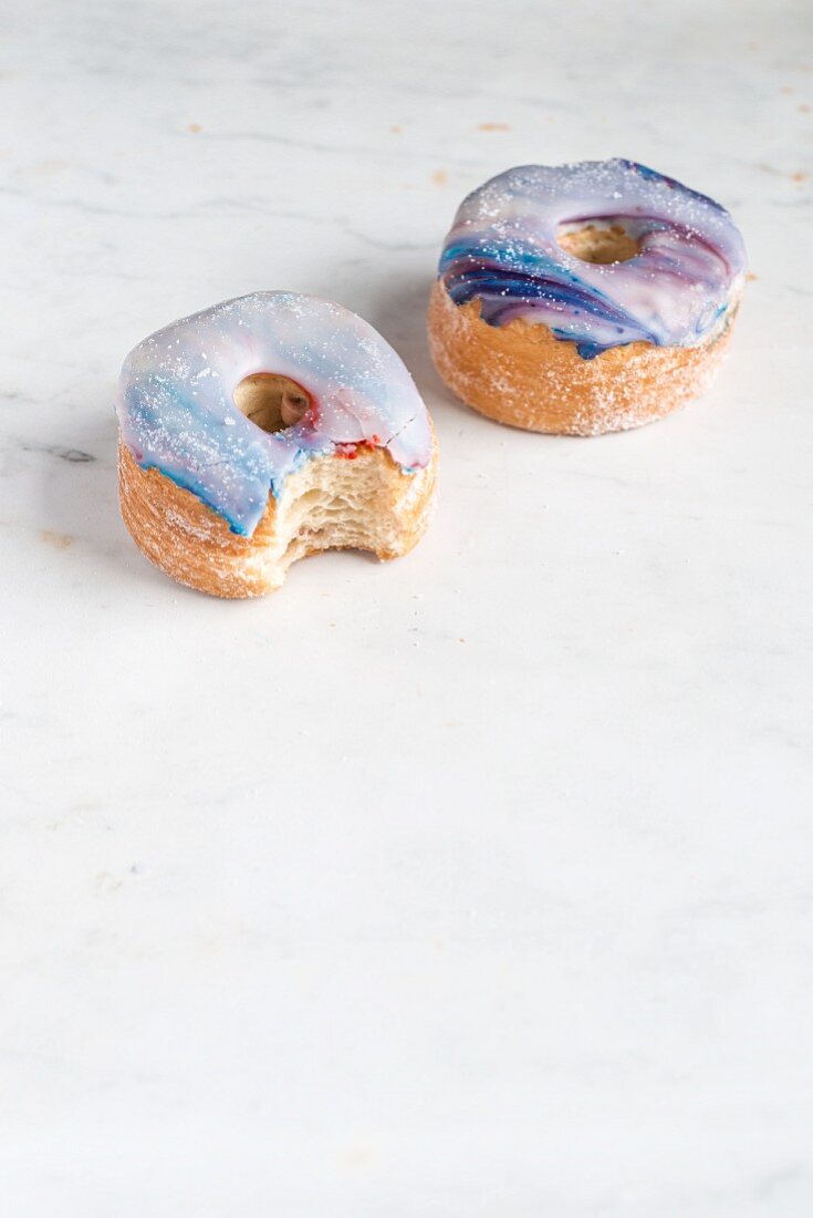 Two galaxy croissant doughnuts with marble glaze, a bite missing