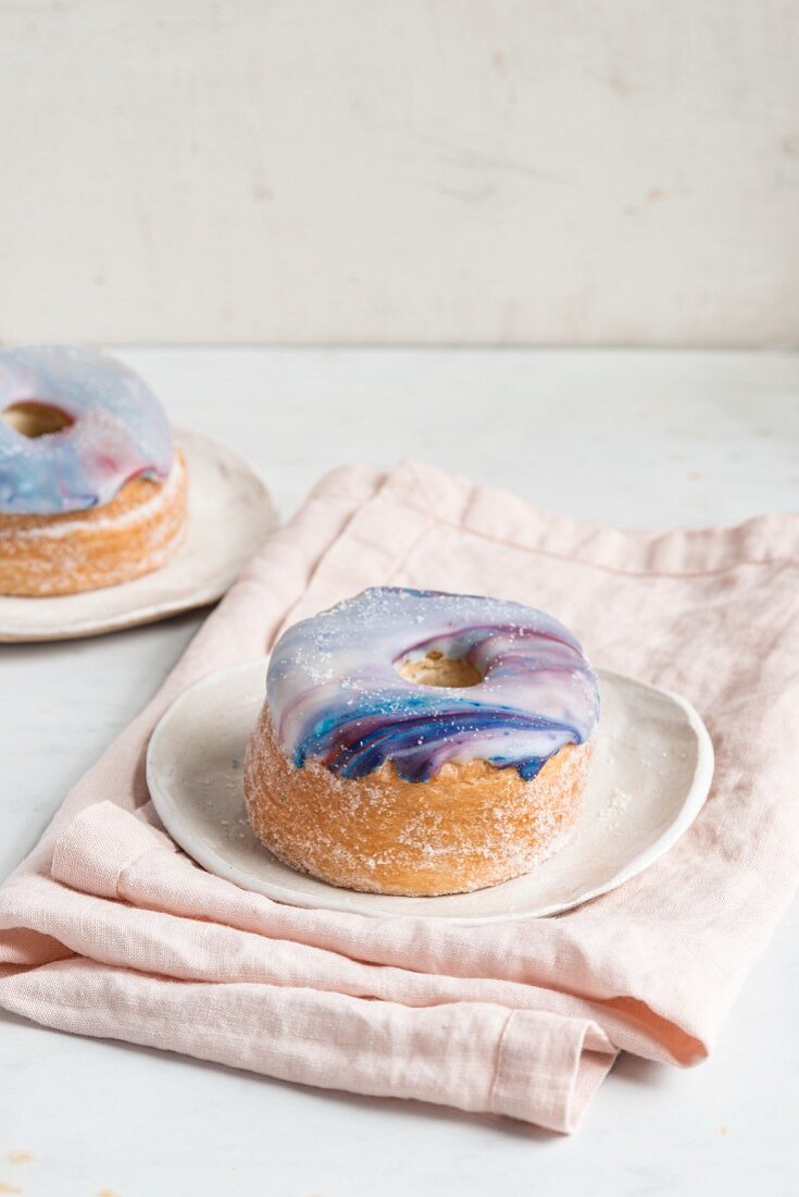 Two galaxy croissant doughnuts with marble glaze on plates
