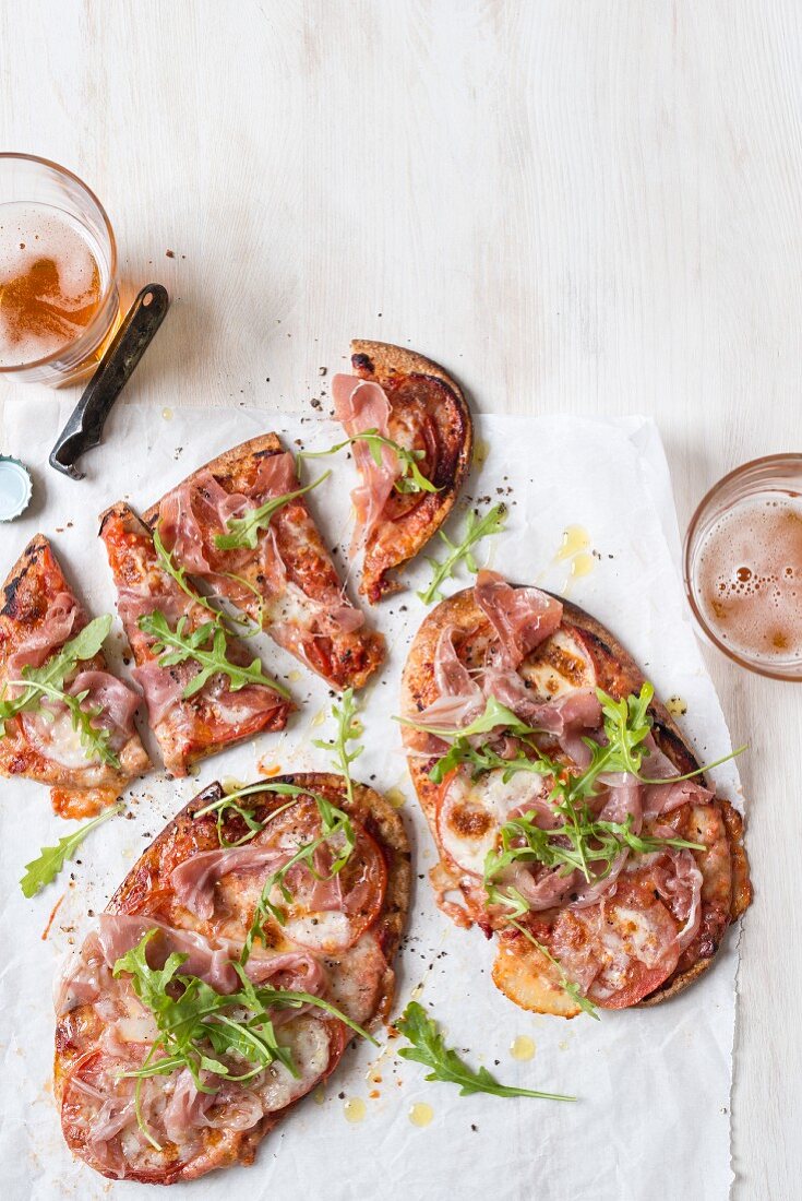 Pizza aus Pitabrot mit geschnittenen Tomaten, Prosciutto, Mozzarella und frischem Rucola