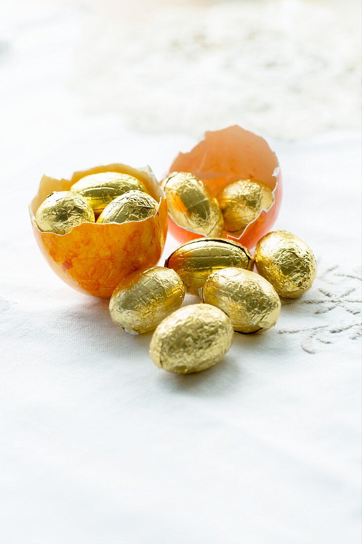 Gefärbte Eierschalen eines leeren Ostereis gefüllt mit Schokoladeneiern in Goldfolie