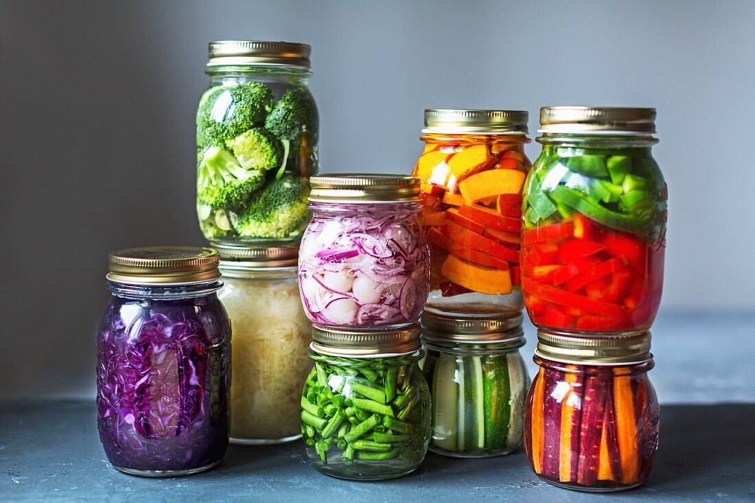 Stacked preserving jars of freshly pickled vegetables in front of a grey background