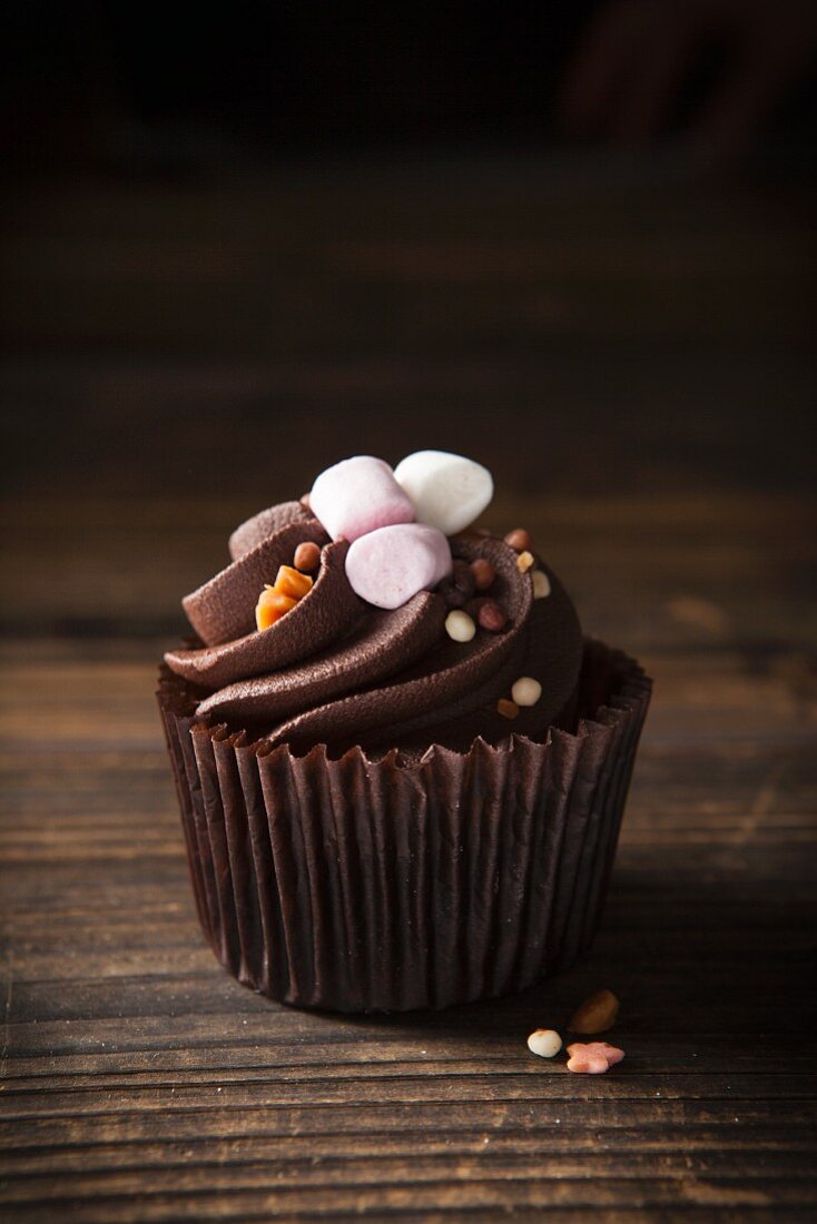 A chocolate cupcake topped with mini marshmallows and toffee sprinkles
