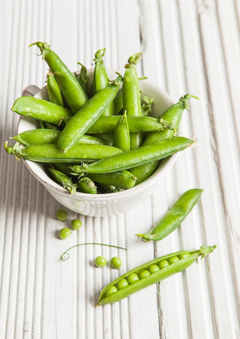 A white bowl full of fresh peas in their pods