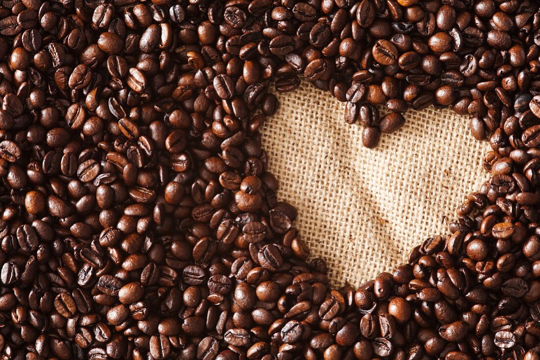 Viele Kaffeebohnen mit ausgeschnittener Herzform auf Jute