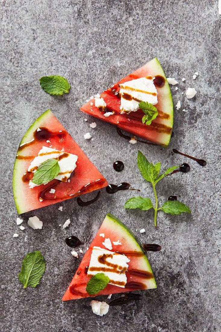 Three slices of fresh watermelon topped with feta cheese, balsamic syrup and fresh mint leaves