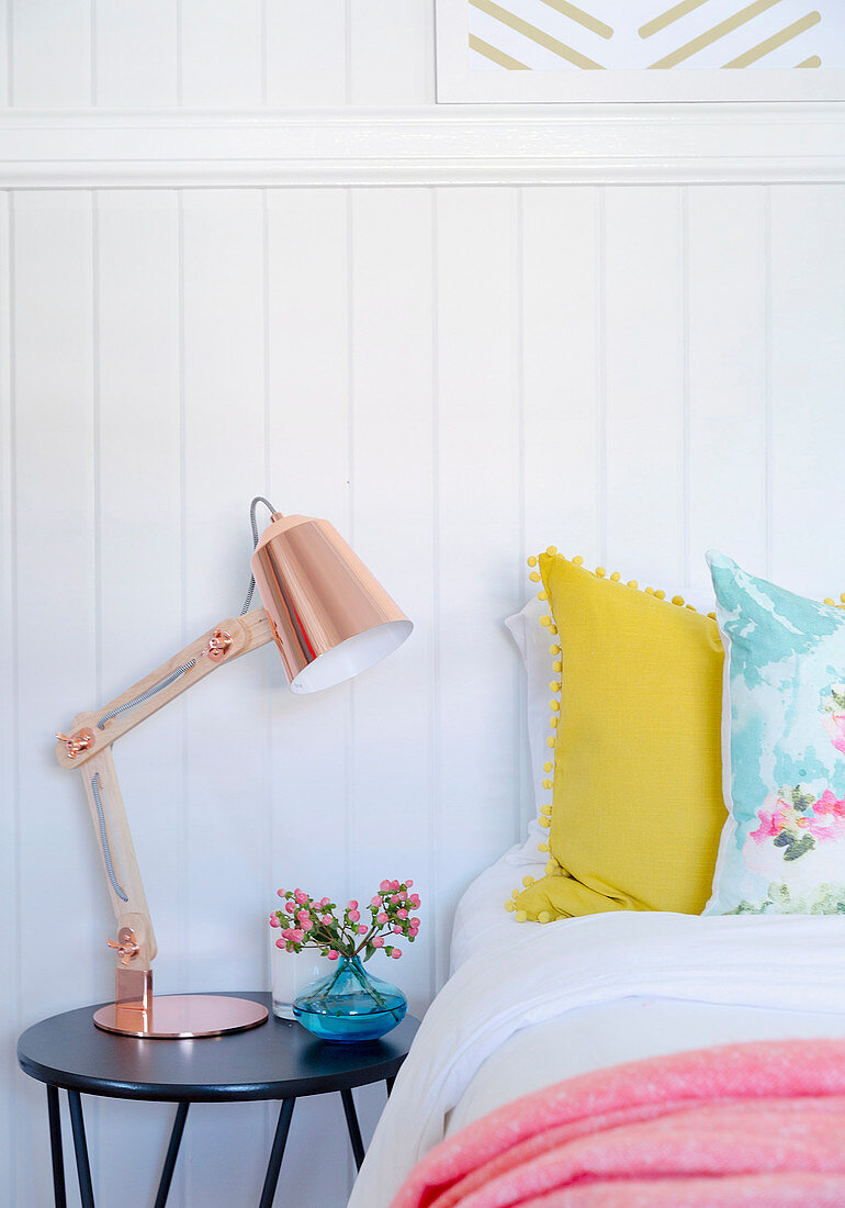 Copper-colored articulated lamp on the bedside table in front of a wooden wall