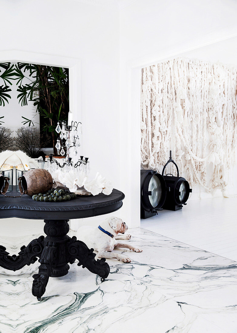 Antique wooden table with candle holder and decorative objects on marble floor, woolen wall hanging in the background