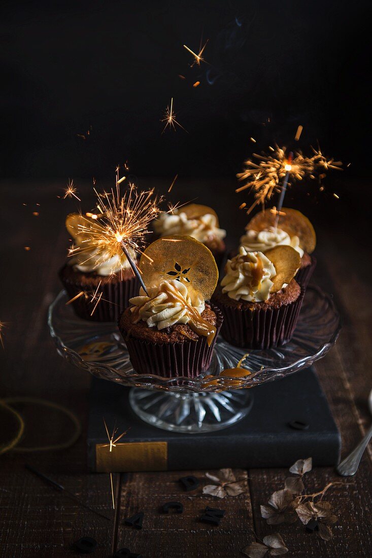 Apfel-Pekannuss-Toffee-Cupcakes mit Apfelchips und Wunderkerze auf Kuchenständer