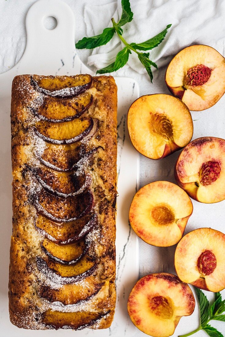 A loaf-shaped peach bread topped with cinnamon and brown sugar on a marble board