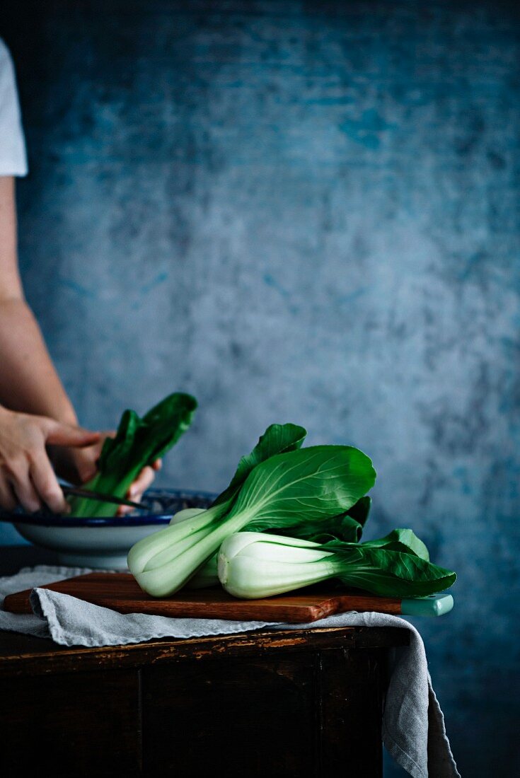 Pak Choi auf Holzbrett und in Schüssel vor blauem Hintergrund