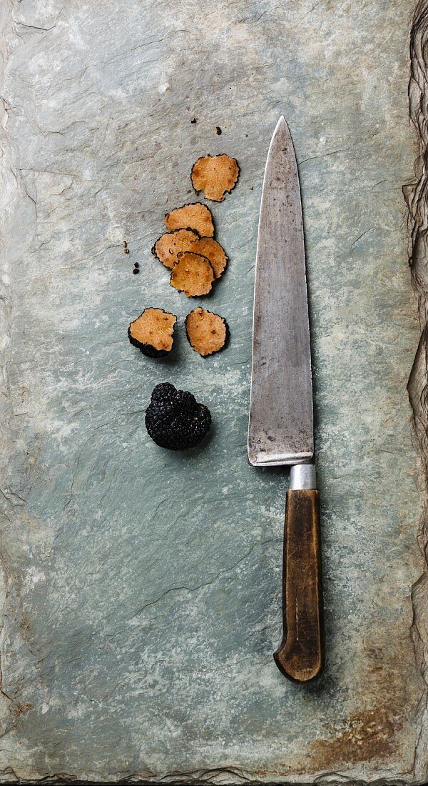 Sliced Black truffle and kitchen knife on stone shale slate background
